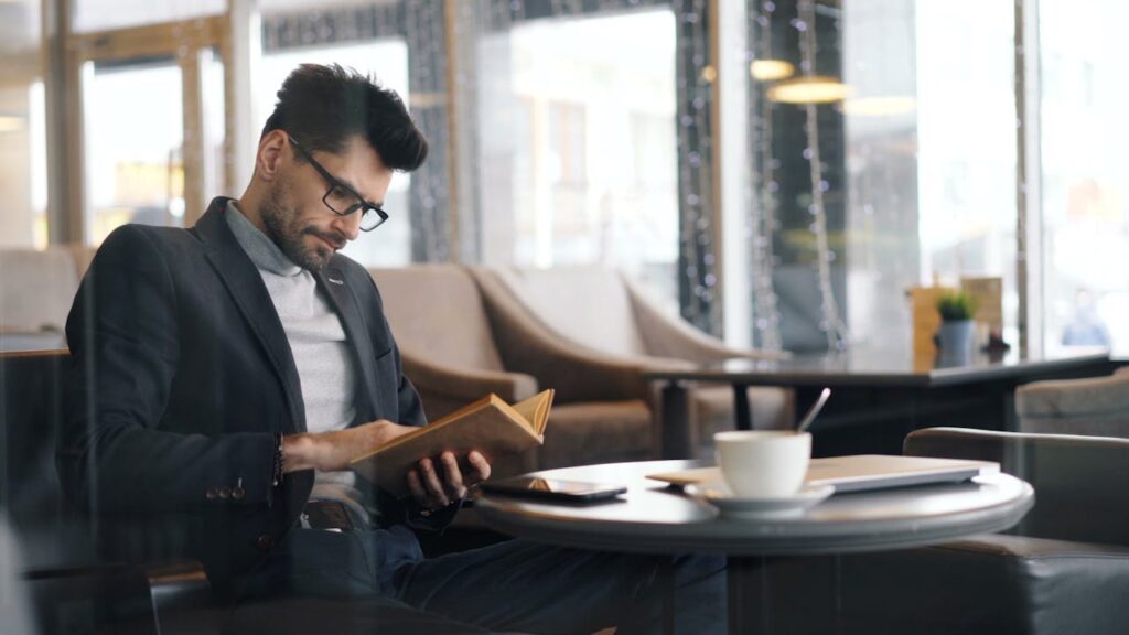 A man engrossed in a book sits in a cafe, his cup of coffee steaming beside him. On the table, a tablet showcases the latest geotechnical innovations, offering insights into civil engineering recruitment trends.